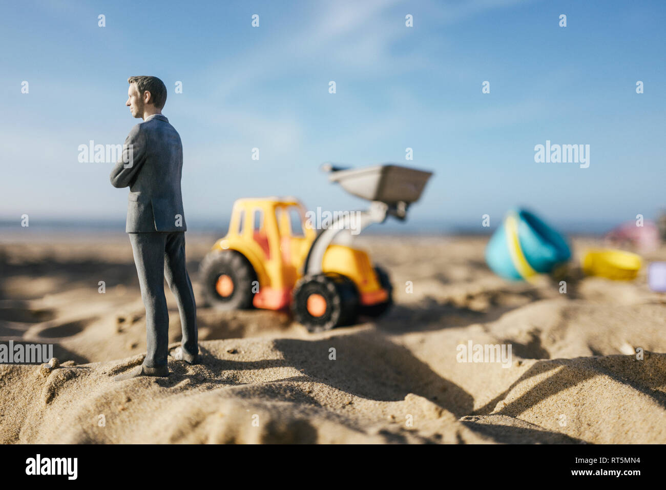 Imprenditore figurina permanente sulla sabbia con toy digger, investimenti in casa di proprietà Foto Stock