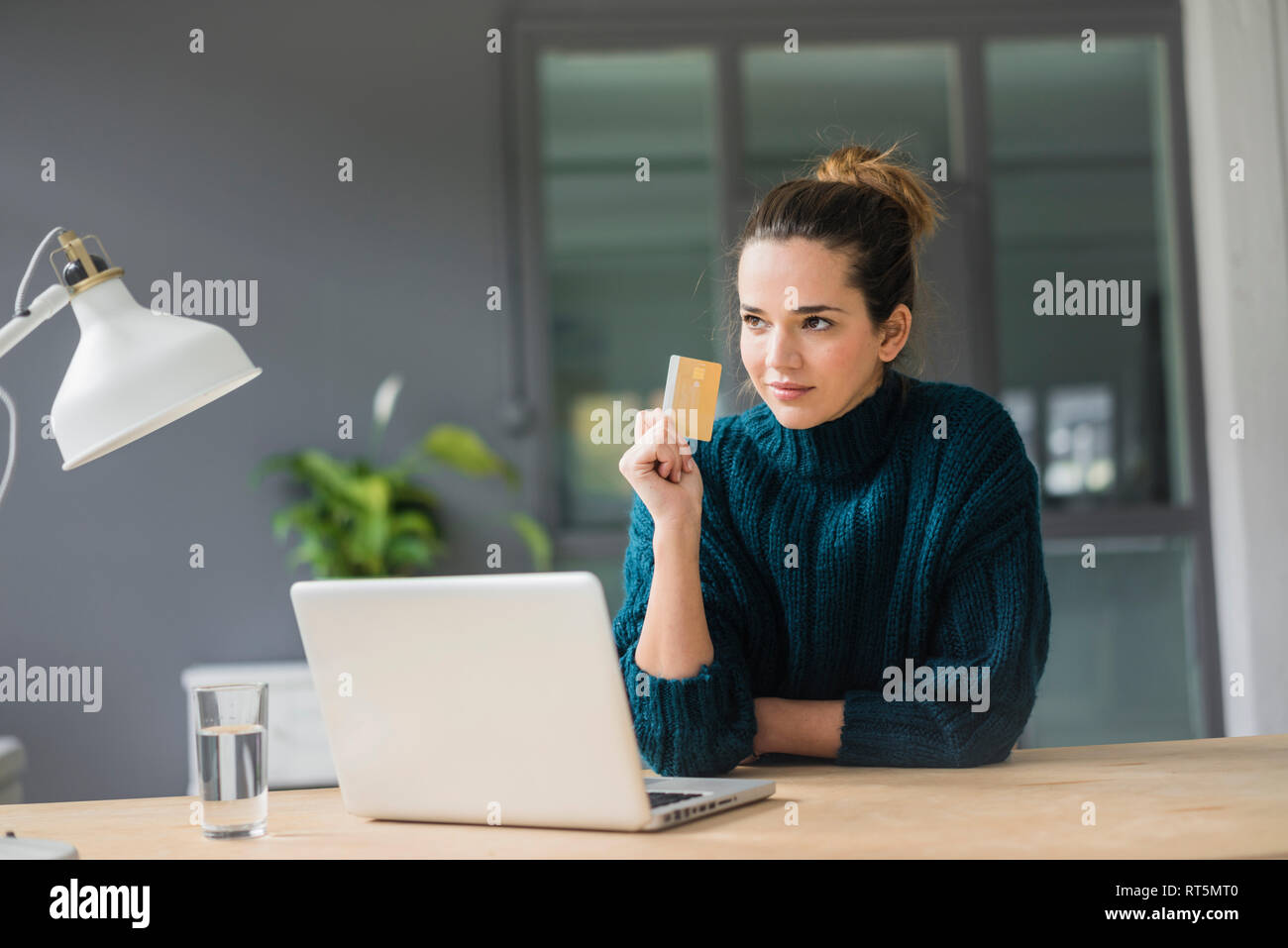 Ritratto di donna di fiducia con il computer portatile e una carta di credito seduto alla scrivania a casa guardando a distanza Foto Stock