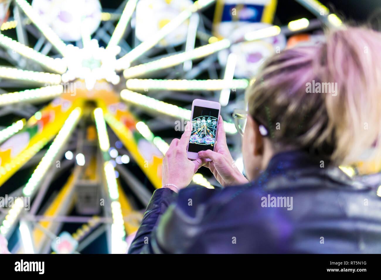 Vista posteriore della donna prendendo foto della grande ruota con lo smartphone al fair Foto Stock