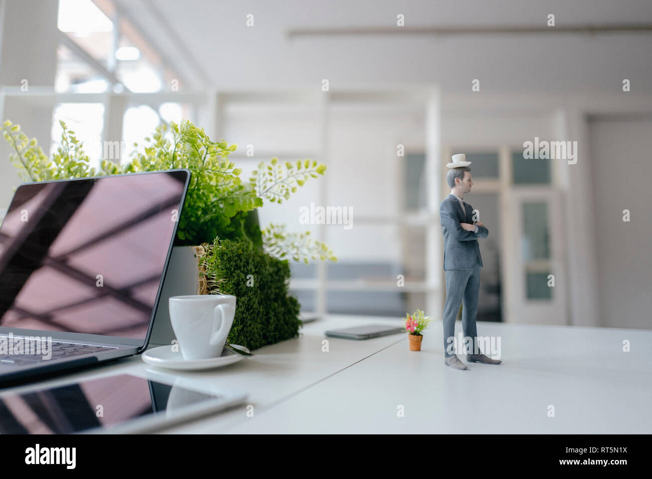 Imprenditore figurina in piedi sulla scrivania, il bilanciamento di una tazza di caffè sulla cima della sua testa Foto Stock