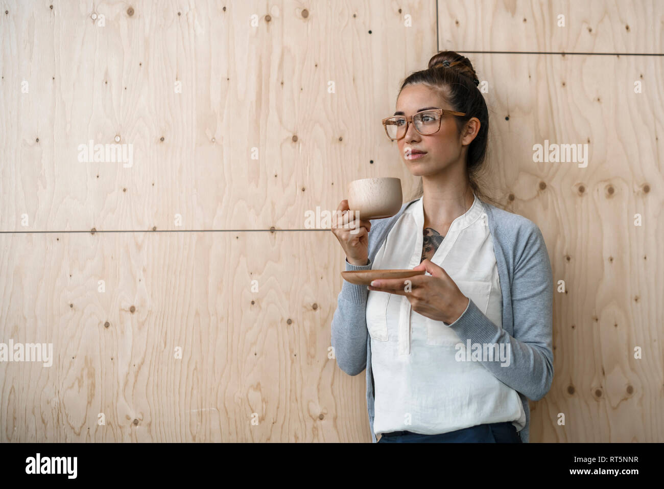 Giovane donna che lavorano in ufficio creativo, prendendo una pausa e di bere il caffè dalla tazza di legno Foto Stock