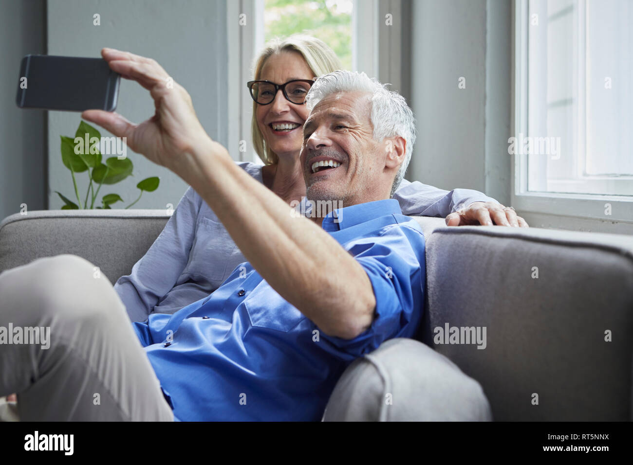 Felice Coppia matura seduti sul divano a casa prendendo un selfie Foto Stock