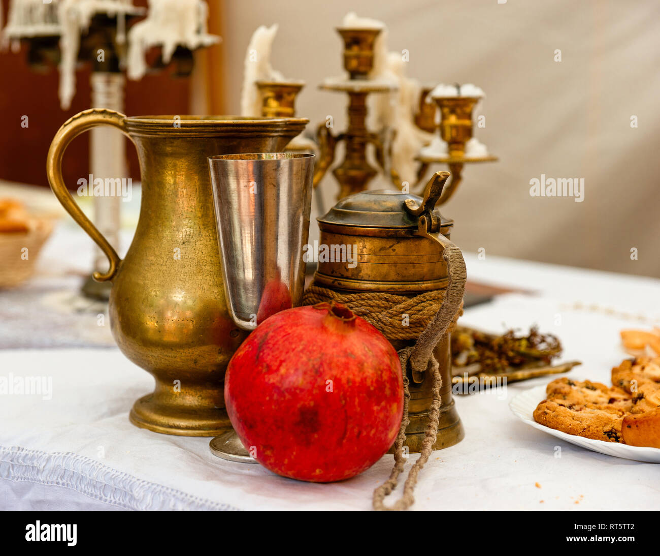 Un rosso frutto di melograno, metallo vintage boccale di birra, un bicchiere di vino e una brocca. Alcune torte fatte in casa sul tavolo, candelabri in background Foto Stock