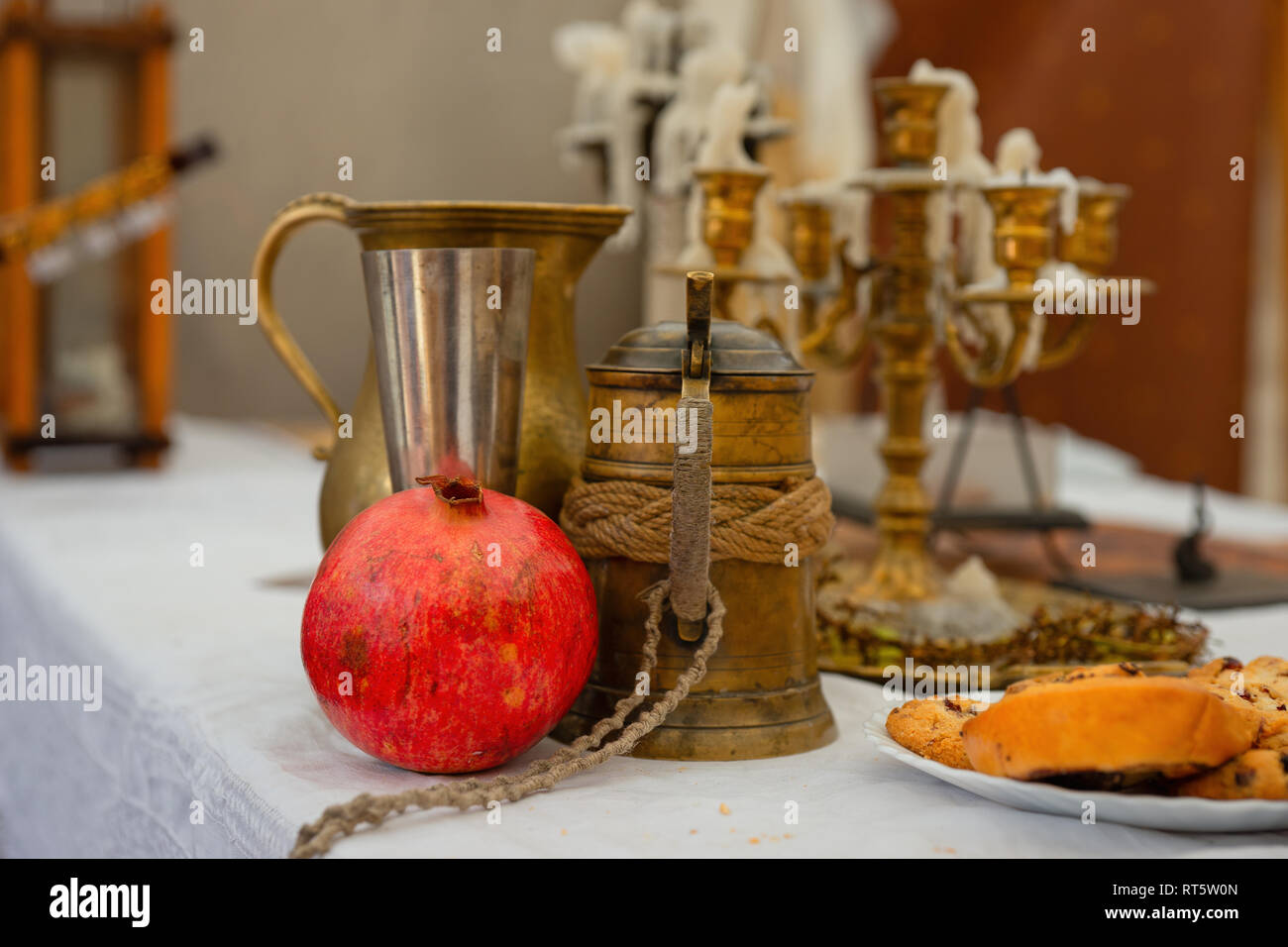 Un rosso frutto di melograno, metallo vintage boccale di birra, un bicchiere di vino e una brocca. Alcune torte fatte in casa sul tavolo, candelabri in background Foto Stock
