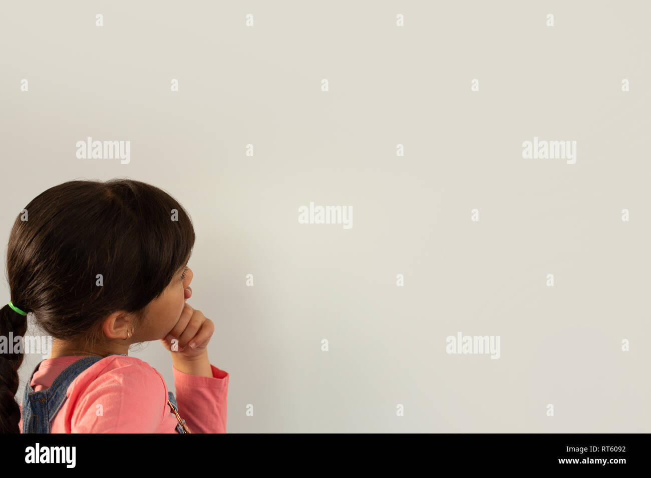 La ragazza con la mano sul mento in piedi contro uno sfondo bianco Foto Stock