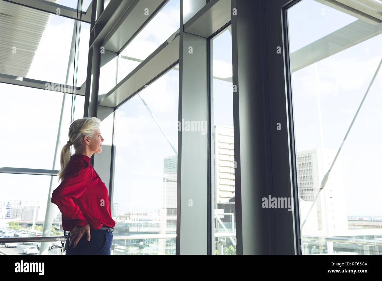 Imprenditrice senior con le mani sul hip guardando attraverso la finestrella in edificio per uffici Foto Stock