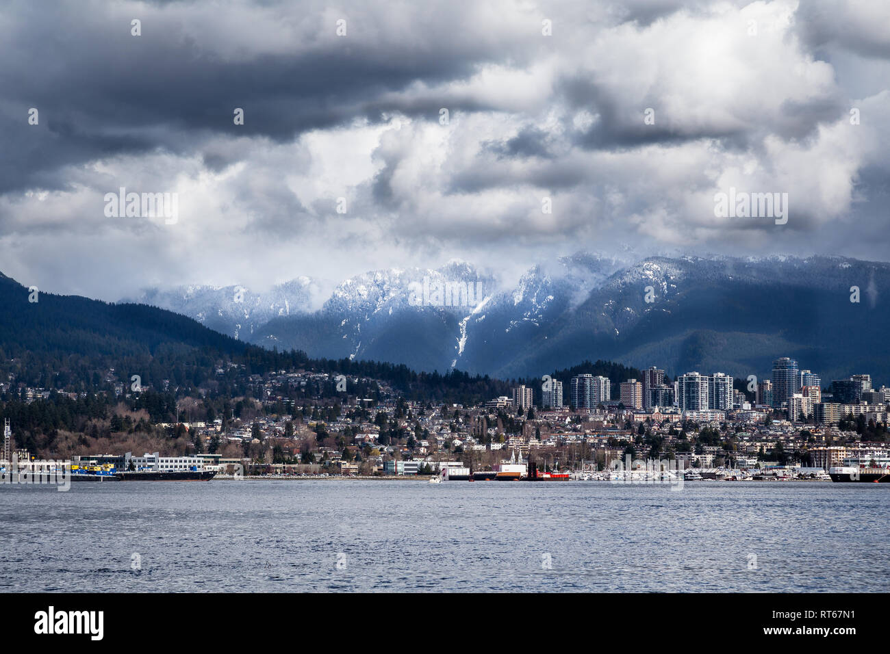 North Vancouver skyline della città con cime coperte di neve dietro, vista dal Parco di Stanley waterfront percorso attraverso il porto , Vancouver, Canada Foto Stock