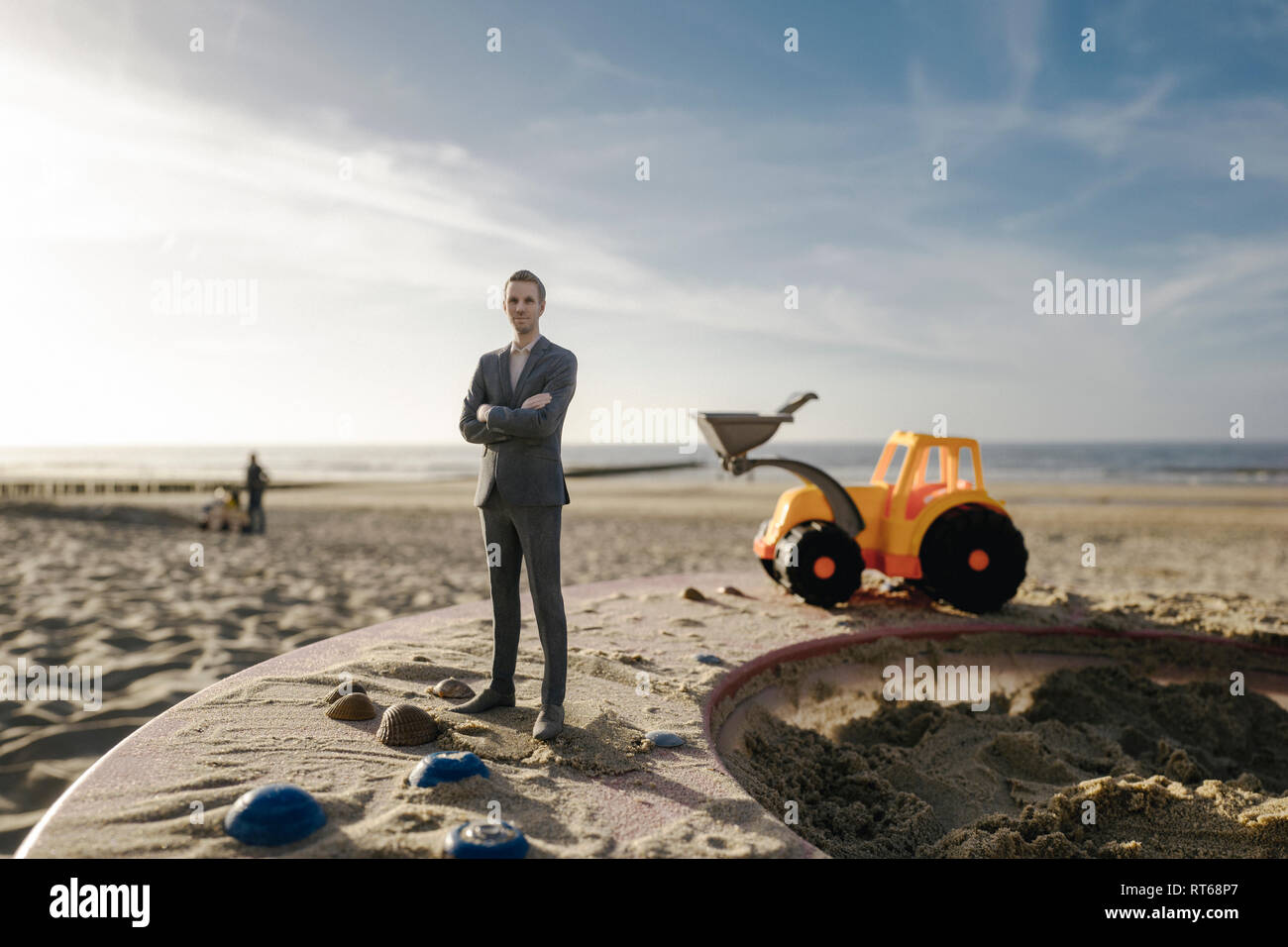 Imprenditore figurina permanente sulla sabbia con toy digger, investimenti in casa di proprietà Foto Stock