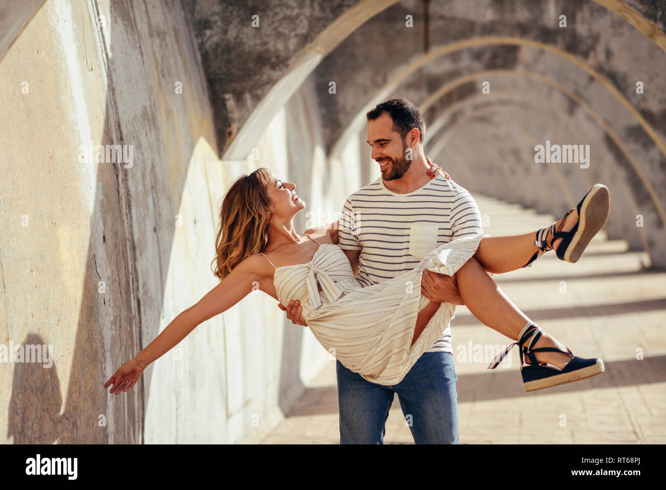 Spagna, Andalusia, Malaga, uomo felice che trasportano ragazza sotto un arco in città Foto Stock