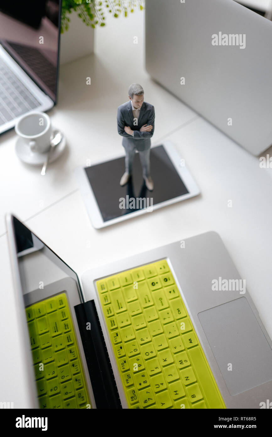 Imprenditore figurina in piedi su una scrivania con i dispositivi mobili e una tazza di caffè Foto Stock