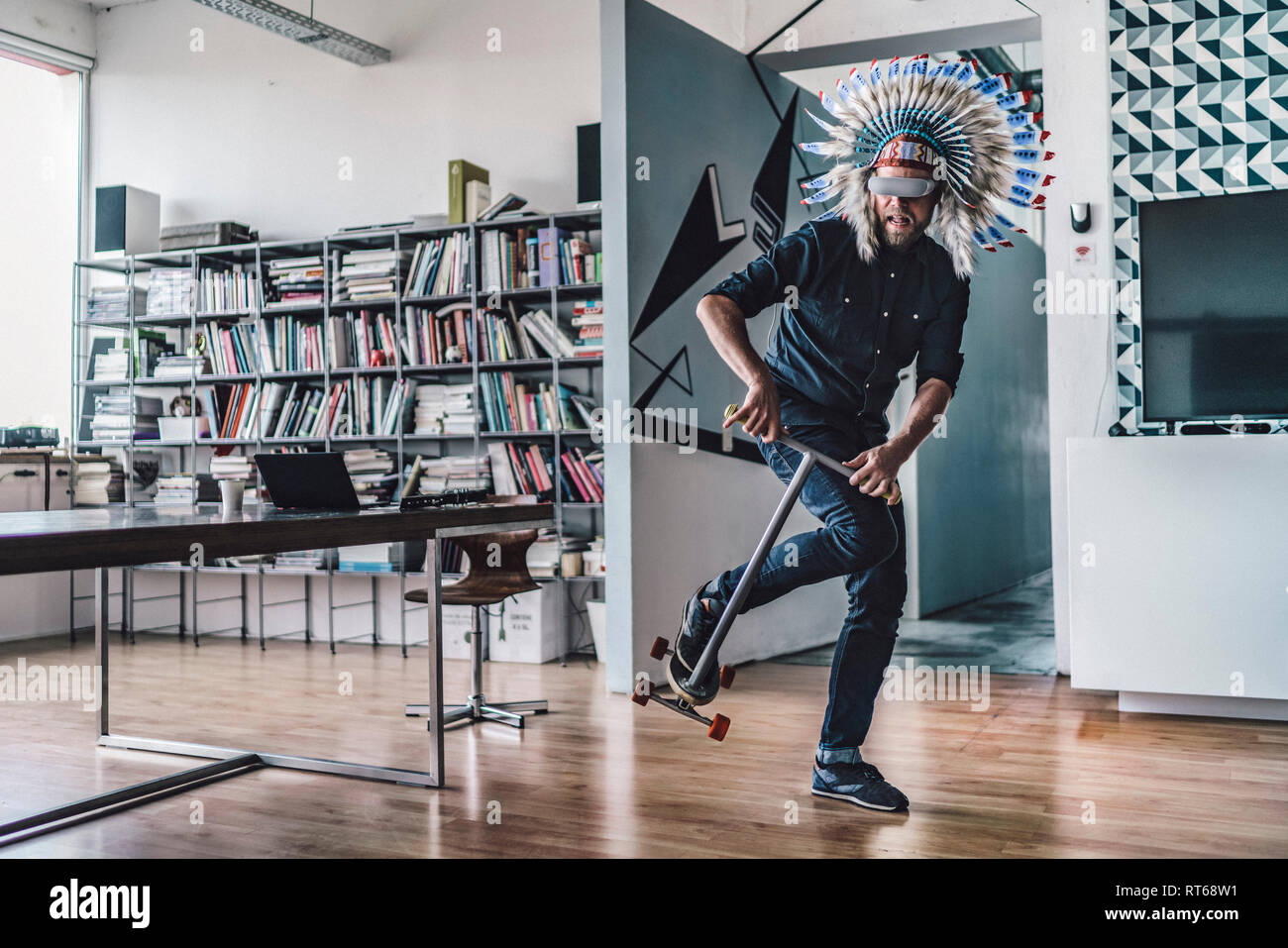 Uomo di indossare copricapo indiano e occhiali VR in ufficio utilizzando kick scooter Foto Stock