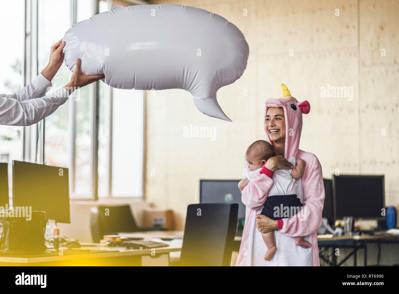 Giovane madre in unicorn onesie, tenendo il suo figlio nelle sue braccia con il discorso di bolla sopra la sua testa Foto Stock