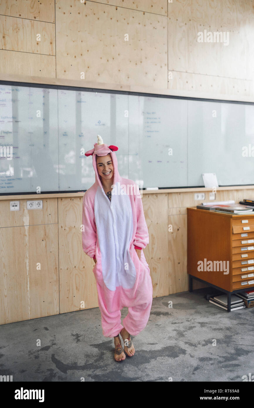 Donna che indossa unicorn onesie, in piedi di fronte a lavagna, ridendo Foto Stock