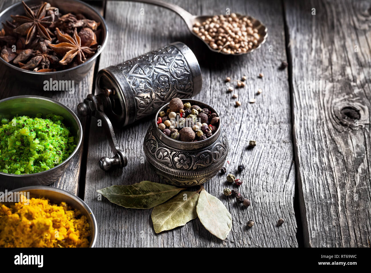 Spezie, pepe di bronzo macinacaffè e cucchiaio con semi di cumino in legno sfondo verde Foto Stock