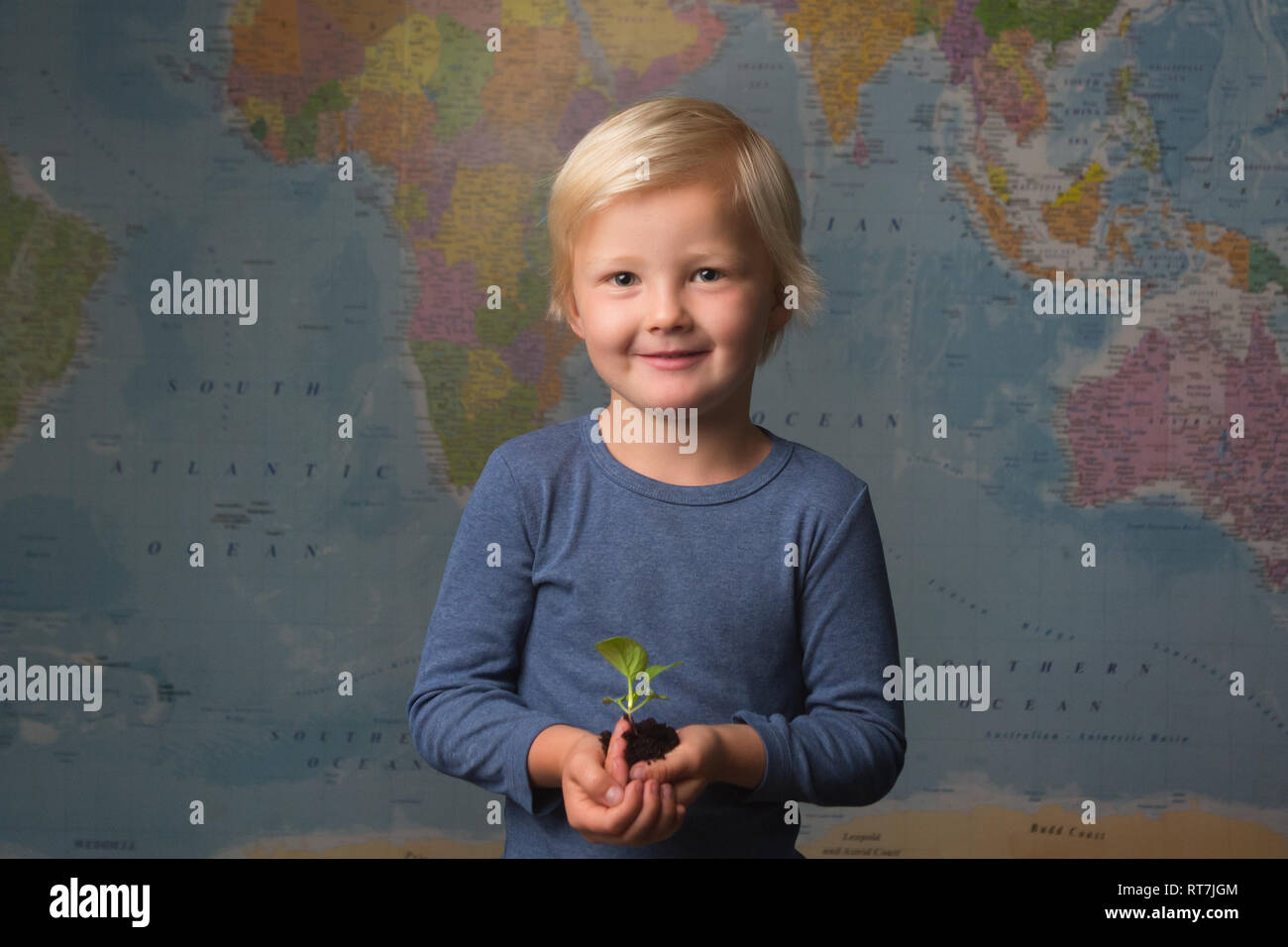 Carino biondo attentamente il bambino tiene una piantina di fronte ad una mappa del mondo Foto Stock