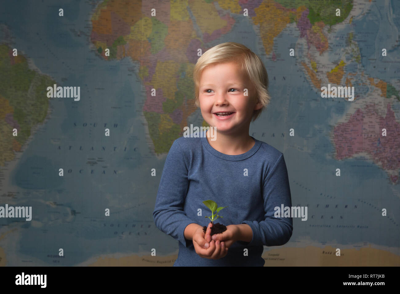 Carino biondo attentamente il bambino tiene una piantina di fronte ad una mappa del mondo Foto Stock