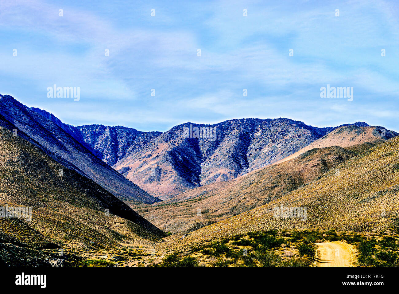 Due versanti formano una piccola valle sotto il luminoso cielo blu con nuvole bianche. Strada sterrata verso valle. Foto Stock