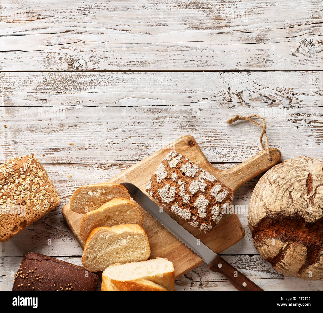 Assortimento di pane fresco su un sfondo di legno. Il bianco e il pane di segale in un sacchetto di carta con Coltello per pane. Concetto di panetteria con copia posto. Foto Stock