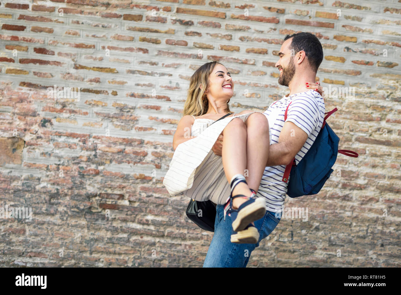 Uomo felice con zainetto fidanzata a un muro di mattoni Foto Stock