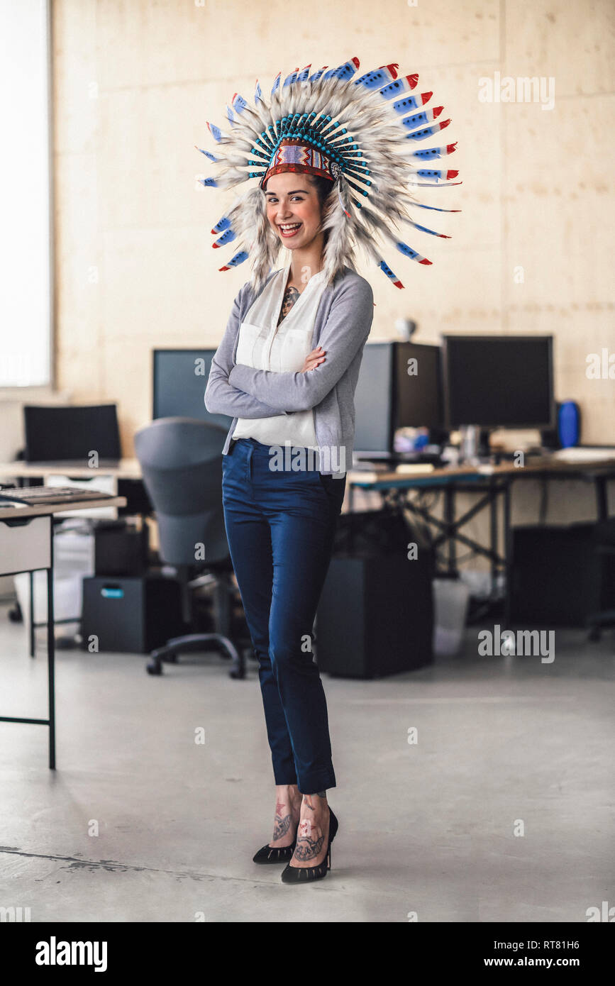 Giovane donna indossare copricapo indiano, stando in ufficio con le braccia incrociate Foto Stock