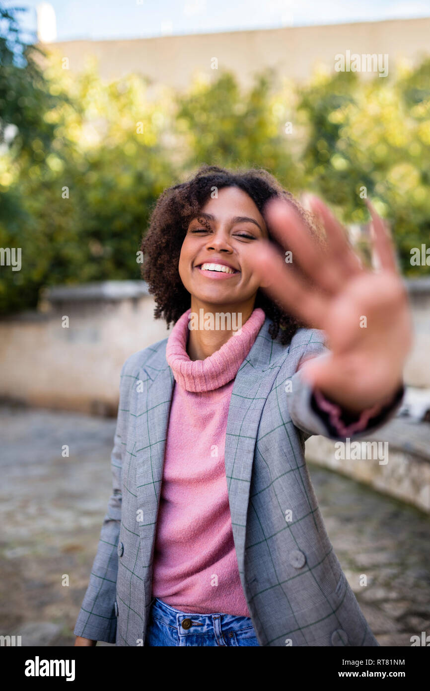 Ritratto di ridere giovane donna alzando la mano Foto Stock