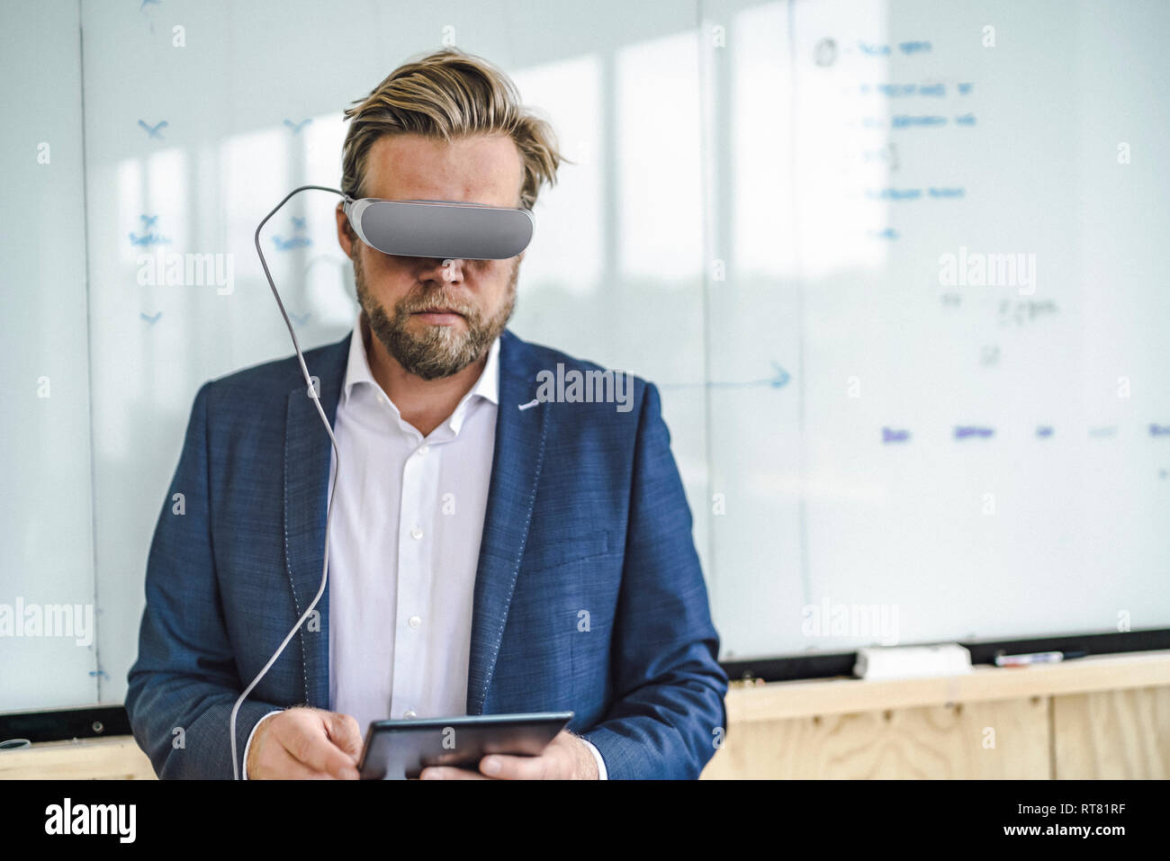 Imprenditore in piedi in ufficio utilizzando occhiali VR e tavoletta digitale Foto Stock