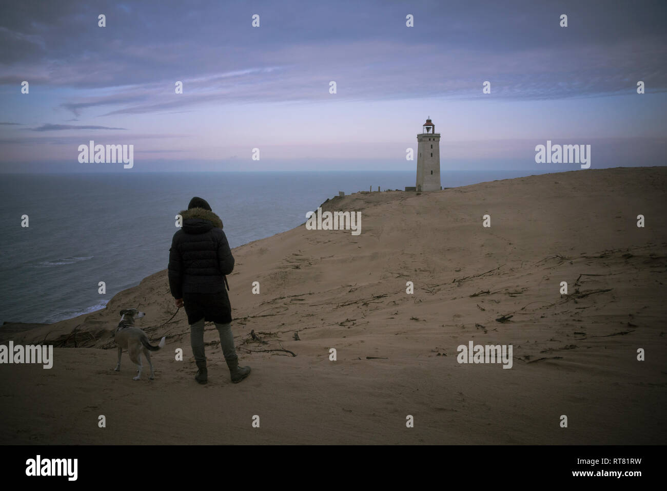 La Danimarca, a nord dello Jutland, vista posteriore dell'uomo con il cane guardando Rubjerg Knude faro ora blu Foto Stock