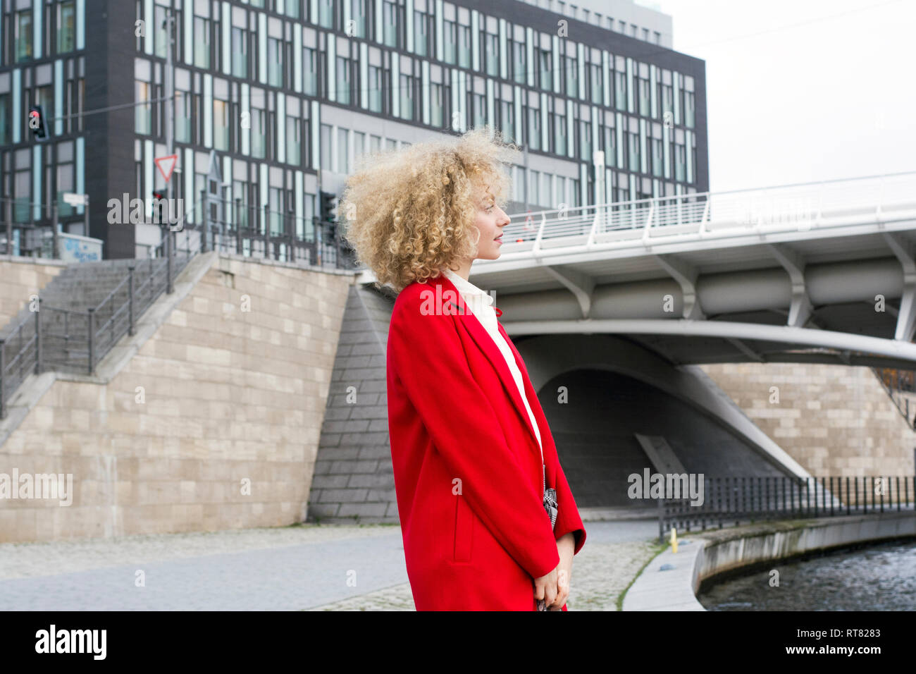 Germania, Berlino, giovane donna bionda con boccoli indossando cappotto rosso Foto Stock