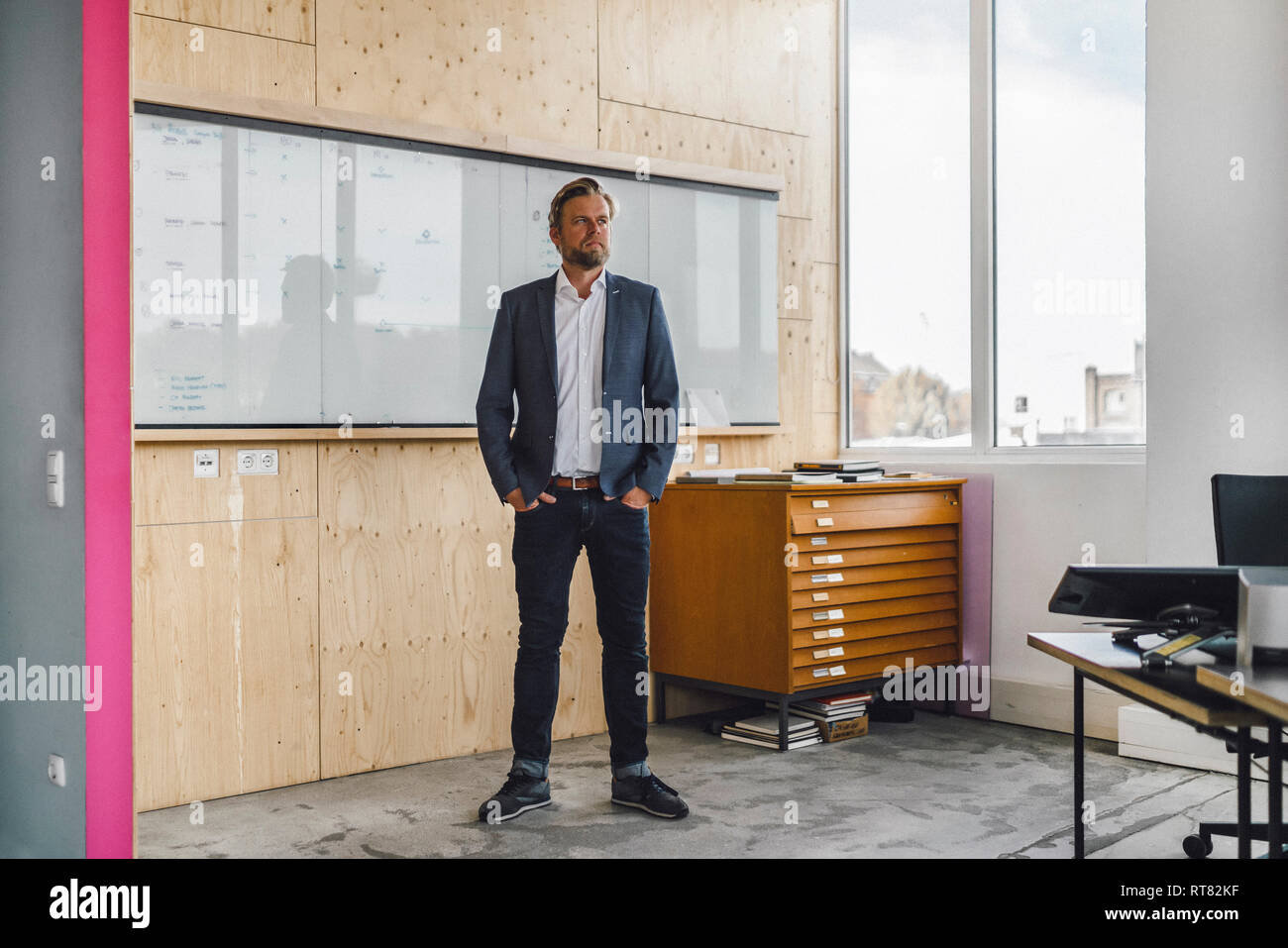 Imprenditore in piedi nel suo ufficio di fronte a whiteboard, con le mani nelle tasche Foto Stock
