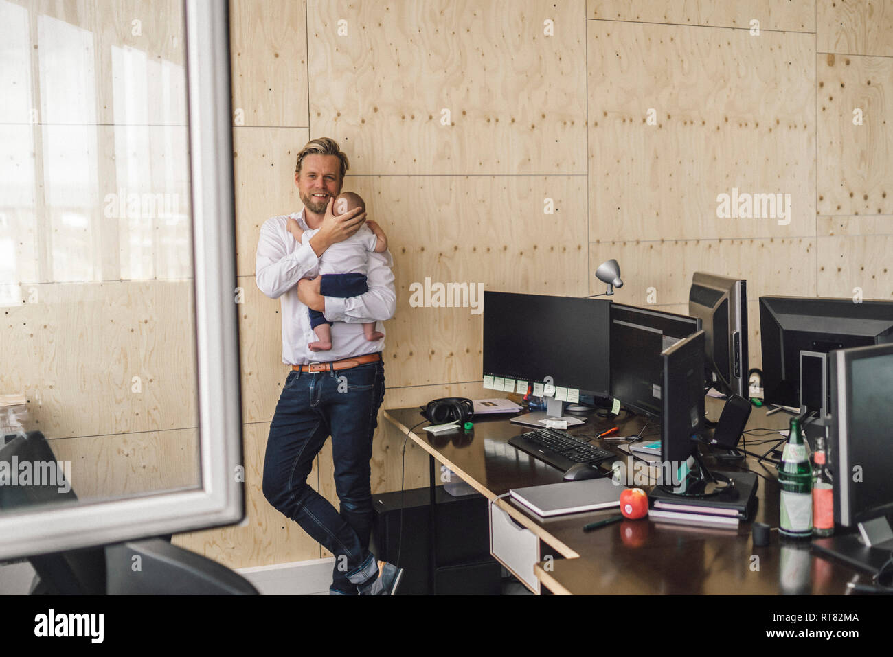 Padre di lavoro in piedi in ufficio, tenendo il suo figlio Foto Stock