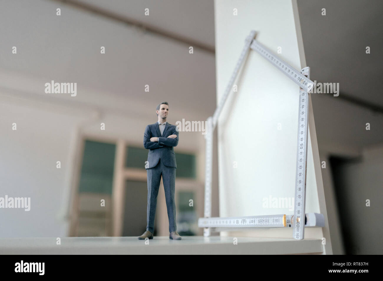 Imprenditore figurina in piedi sulla tavola con pocket regola, sagomando una casa Foto Stock