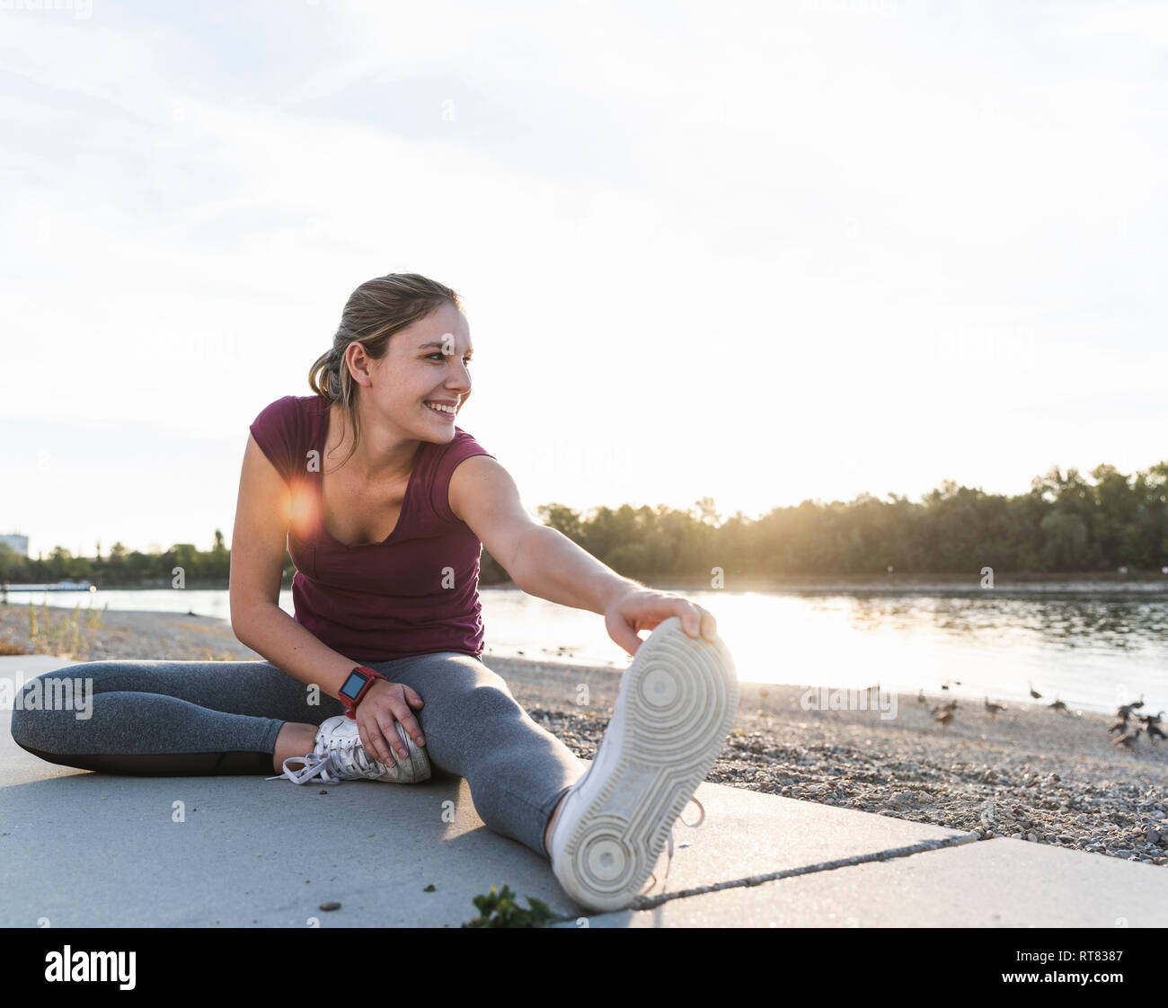 Giovane donna seduta su un terreno presso il fiume, il riscaldamento per la formazione Foto Stock