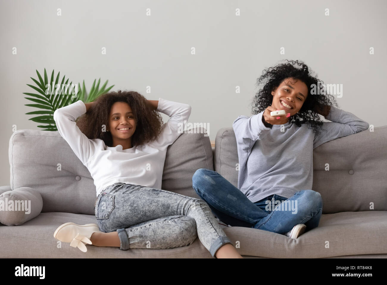 Madre africana tenendo premuto il telecomando in appoggio con la figlia sul lettino Foto Stock