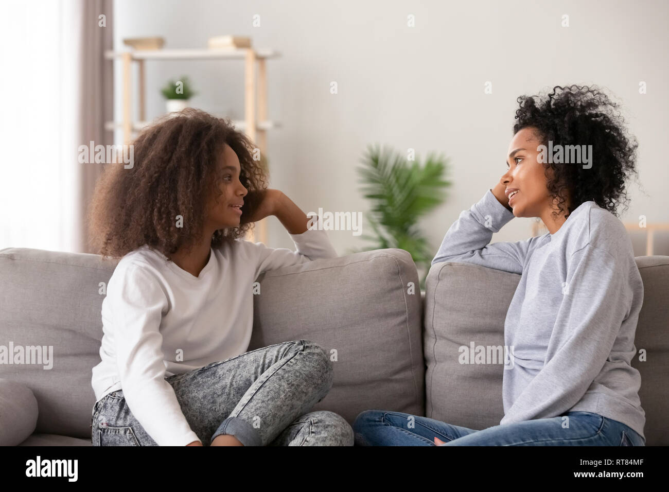 I giovani africani mom ascolto figlia teenager seduti sul divano insieme Foto Stock