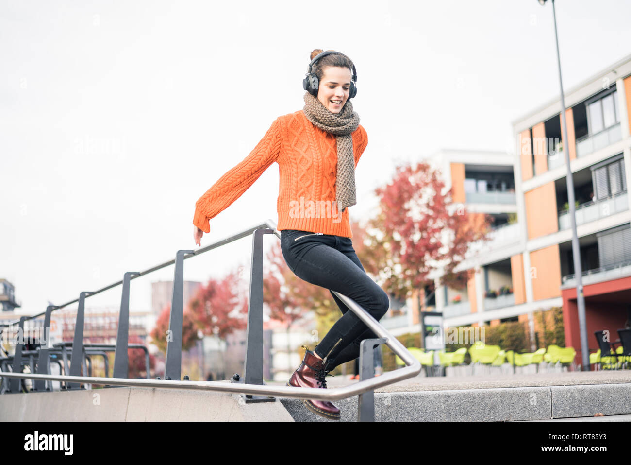 Ritratto di donna ridere con cuffie cordless lo scorrimento verso il basso una ringhiera Foto Stock