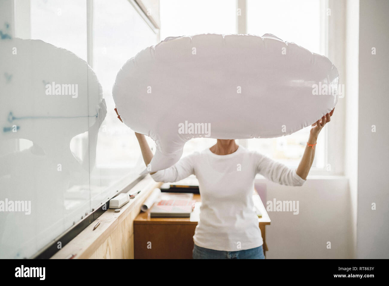 Donna in piedi in ufficio, tenendo gonfiabile di fumetto discorso davanti al suo volto Foto Stock