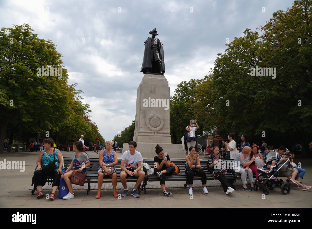 Persone a sedersi su una panchina di fronte alla statua di bronzo di James Wolfe, Victor del Québec, in Greenwich, Londra, Regno Unito. Foto Stock