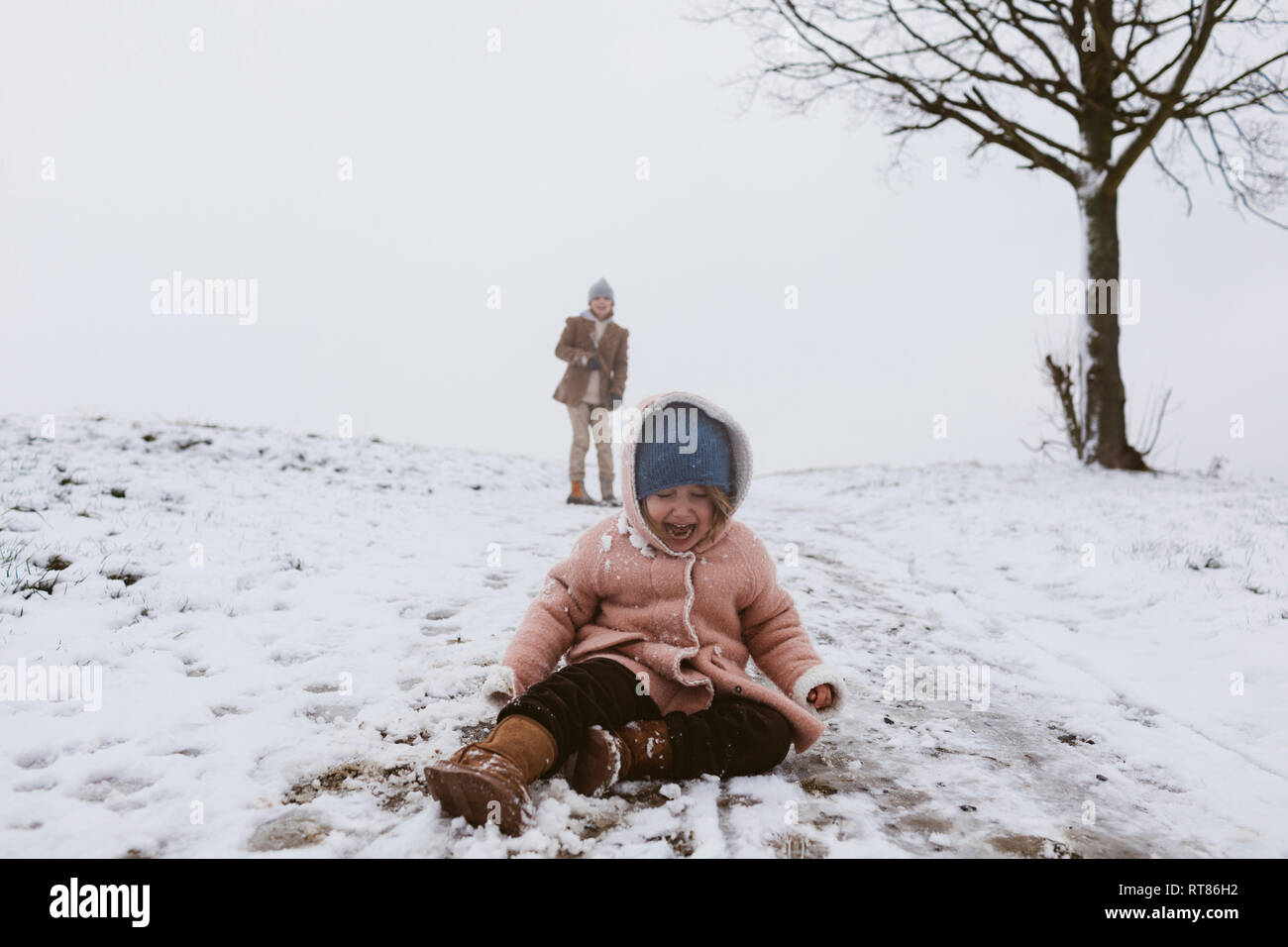 Ragazza che piange sulla coperta di neve prato con il fratello in background Foto Stock