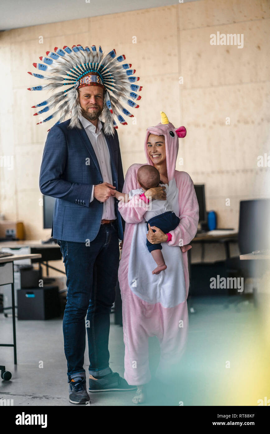 L uomo e la donna vestita come Indiani e unicorn, stando in ufficio, donna tenendo il bambino nelle braccia Foto Stock