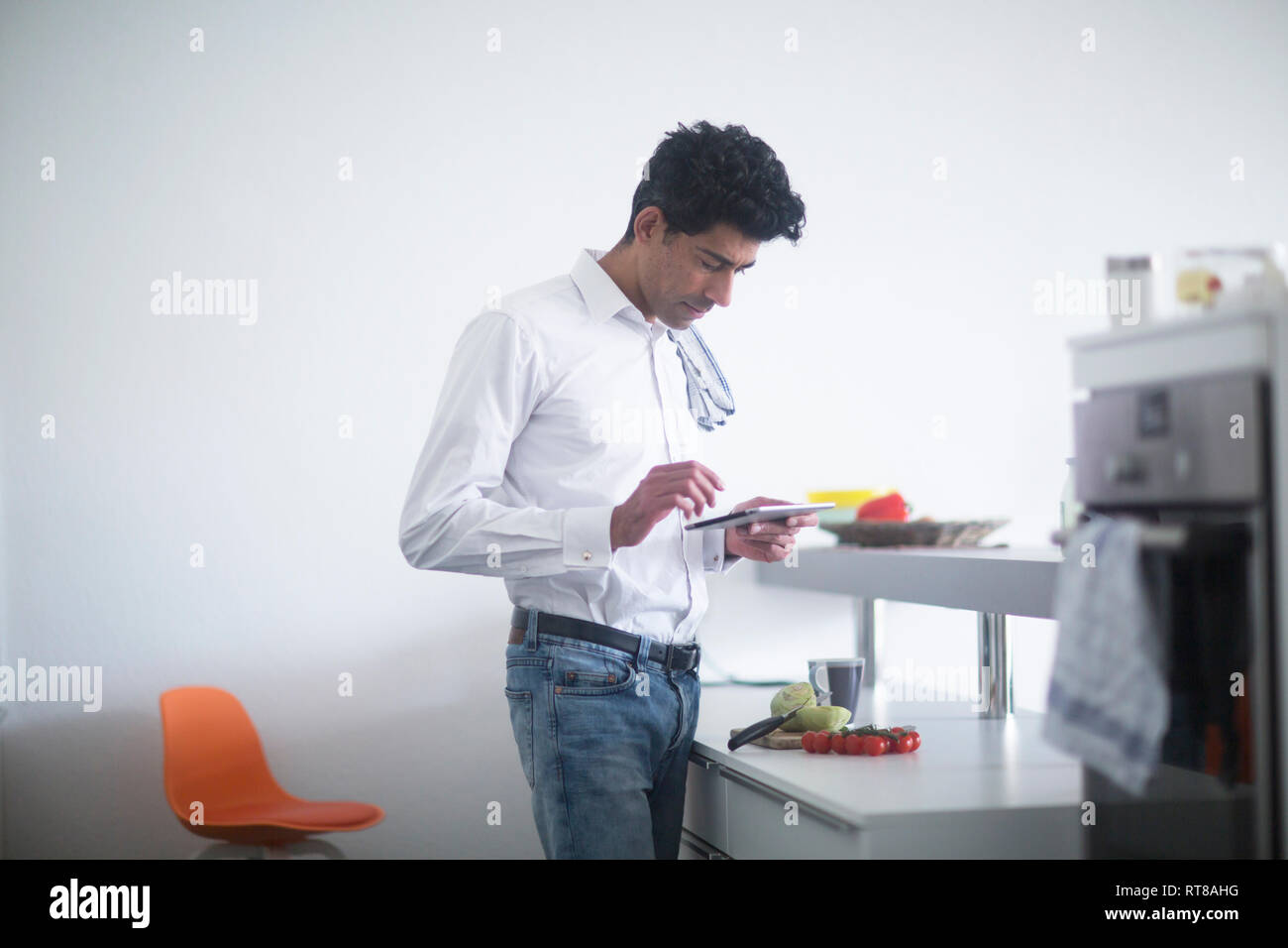 Uomo in piedi in cucina ricetta di lettura sulla sua tavoletta digitale Foto Stock