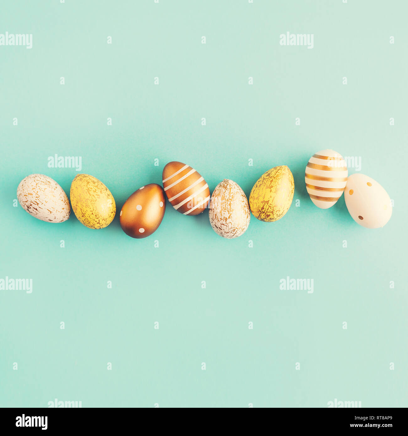 Piatto di laici Golden Uova di Pasqua nella riga posta su sfondo turchese. Pasqua dello sfondo o il concetto di pasqua. Foto Stock