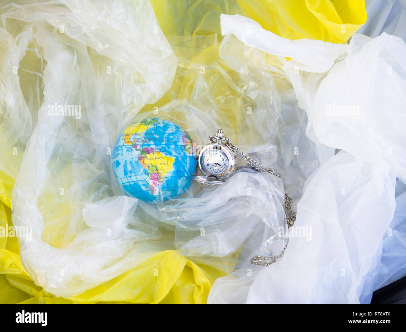 Un globo terrestre o pianeta terra tra i rifiuti e i sacchetti di plastica con un orologio analogico accanto ad essa. Concetto di ecologia Foto Stock