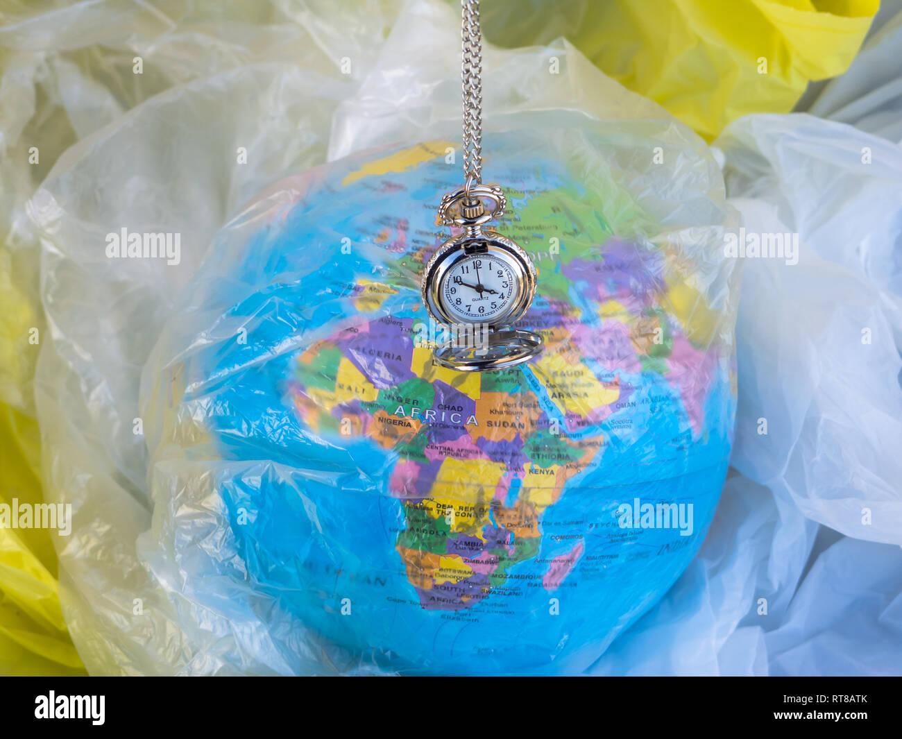 Un globo terrestre o pianeta terra tra i rifiuti e i sacchetti di plastica con un orologio analogico accanto ad essa. Concetto di ecologia Foto Stock