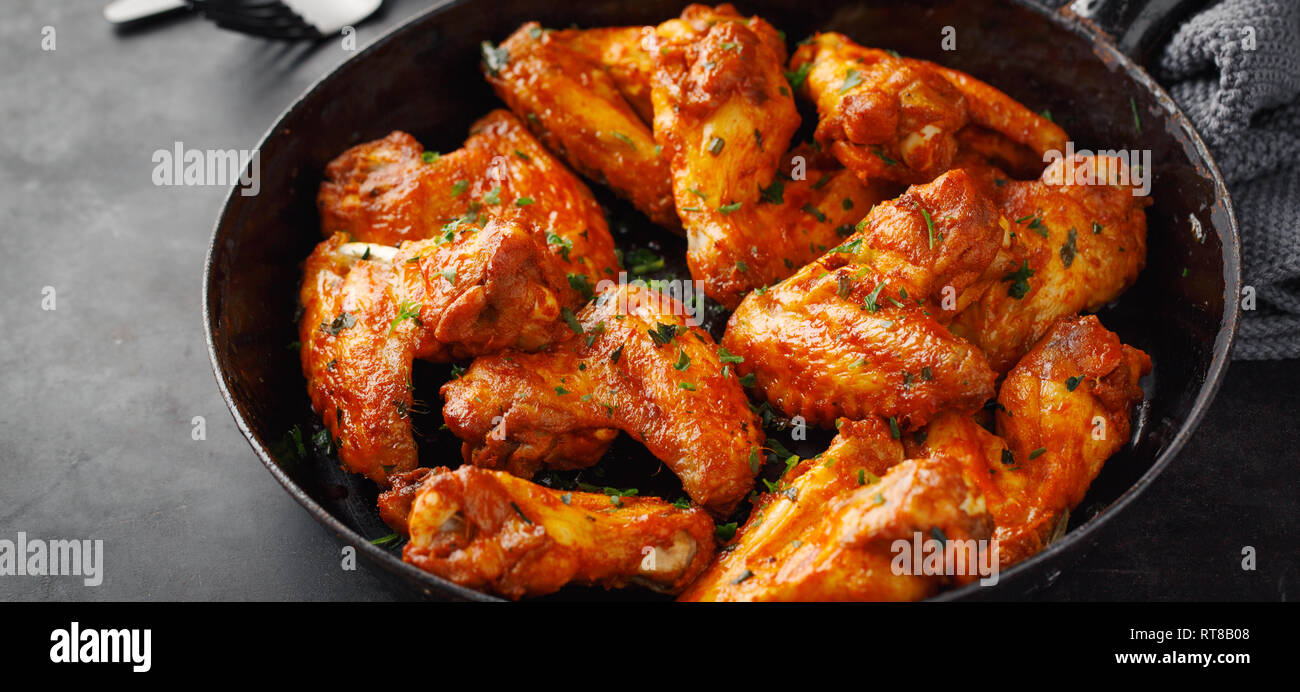 Gustosa ali di pollo al forno o alla griglia in salsa servita sulla teglia. Sfondo scuro. Orizzontale. Foto Stock