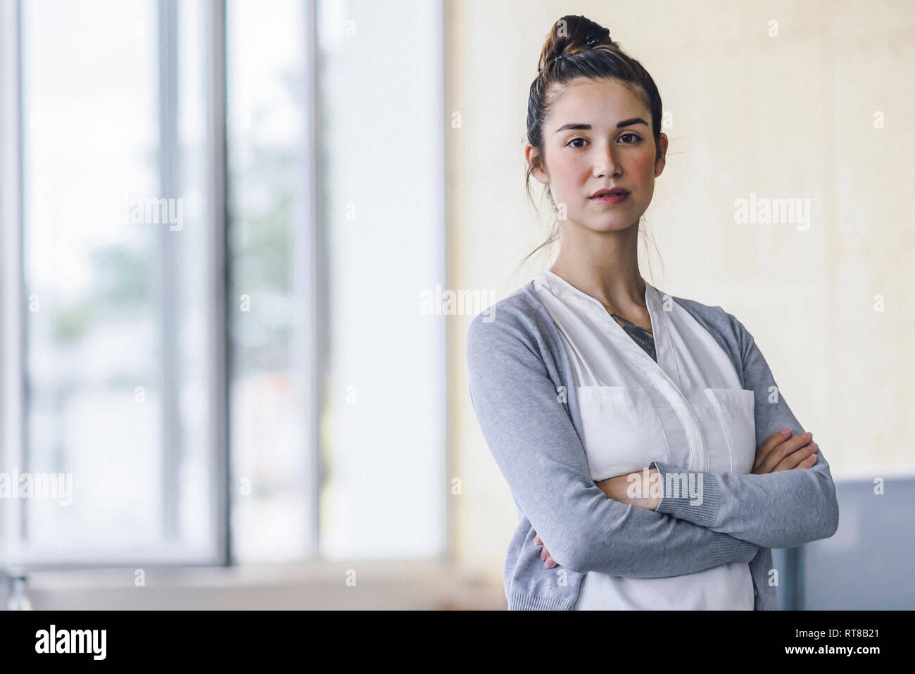 Ritratto di una giovane e bella donna in piedi in ufficio con le braccia incrociate Foto Stock