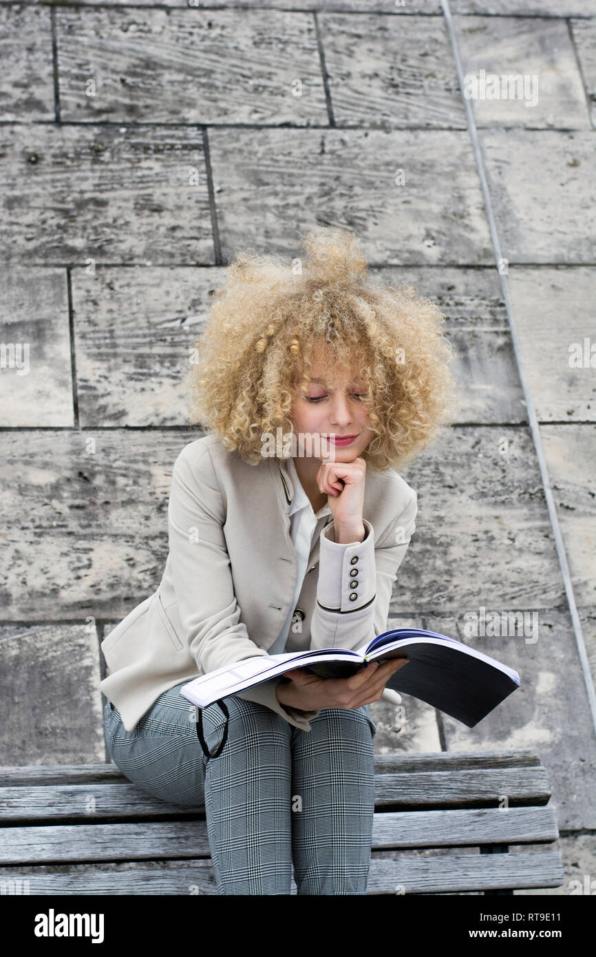Ritratto di donna bionda con boccoli seduta sul banco di lavoro guardando opuscolo Foto Stock