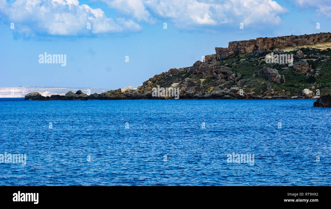 La baia del Mediterraneo di Gneina Bay sull'isola di Malta. Il suo fine campo e l'isola di Gozo nel lontano sullo sfondo contro un cielo blu. Foto Stock