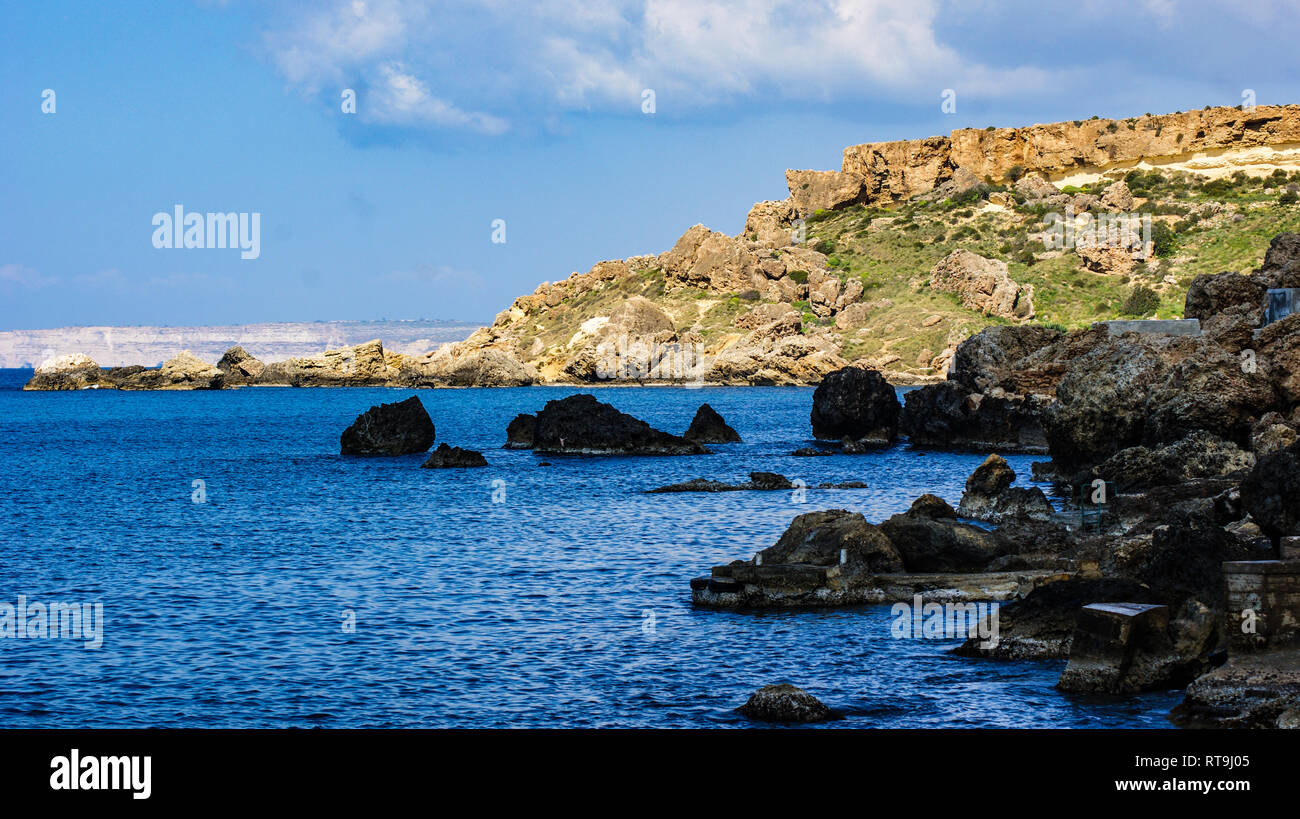 La baia del Mediterraneo di Gneina Bay sull'isola di Malta. Il suo fine campo e l'isola di Gozo nel lontano sullo sfondo contro un cielo blu. Foto Stock