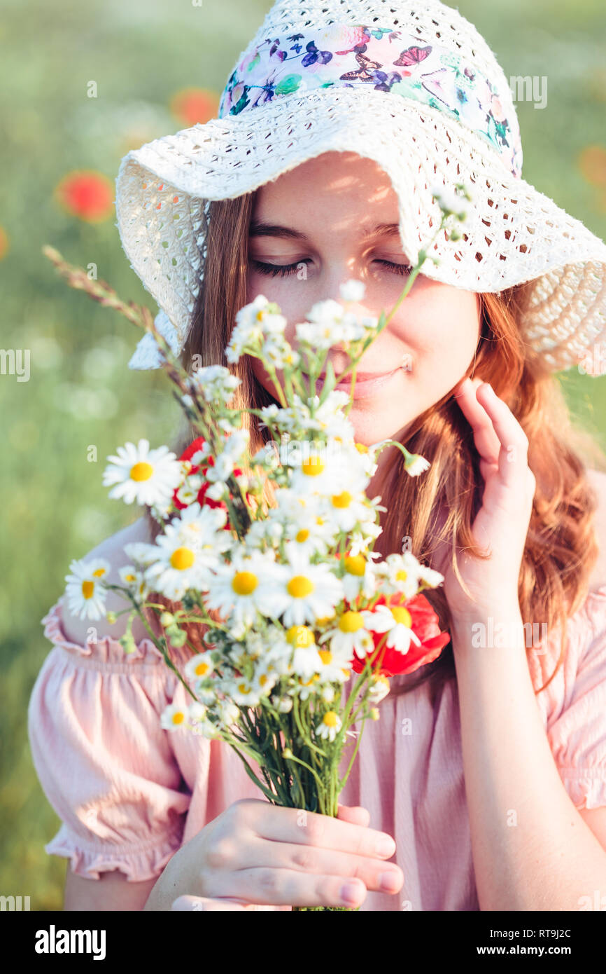 Beautieful giovane ragazza nel campo dei fiori selvatici. Ragazza adolescente picking i fiori di primavera nel prato, tenendo bouquet di fiori. Lei indossa hat Foto Stock