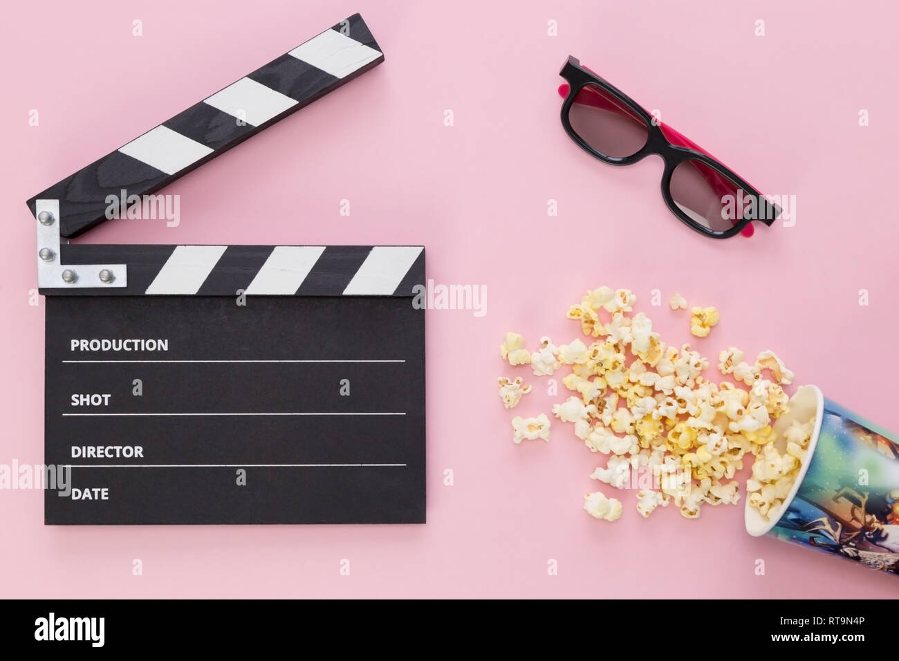 Clapperboard nero, bicchieri e una tazza con popcorn sparsi su un sfondo rosa Foto Stock